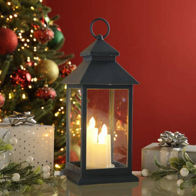 Christmas battery operated candles in lantern with Christmas tree in background with gifts