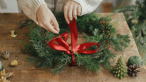 Woman Decorating Plain Christmas Wreath with Red Ribbon and Berries