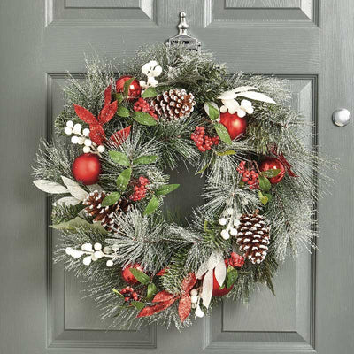 snowy christmas wreath with pine cones, red leaves and berries on a door